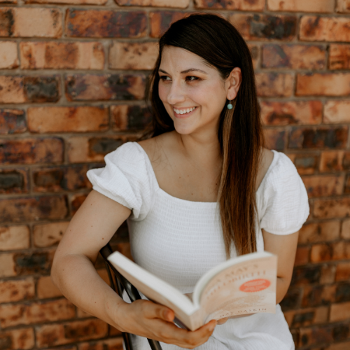 Woman holding a book against a brick wall