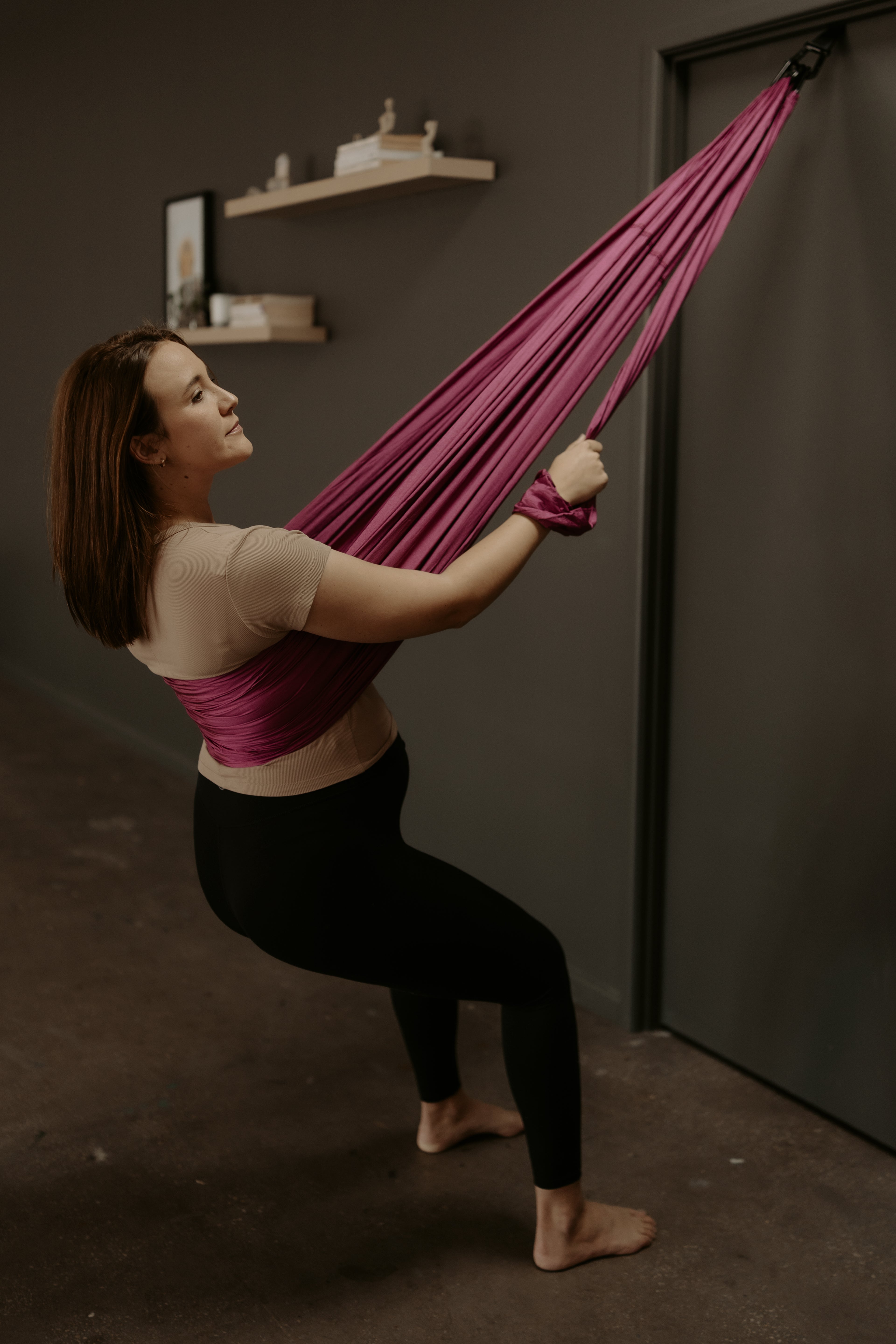 Woman using a pink purple birth sling against a dark wall.