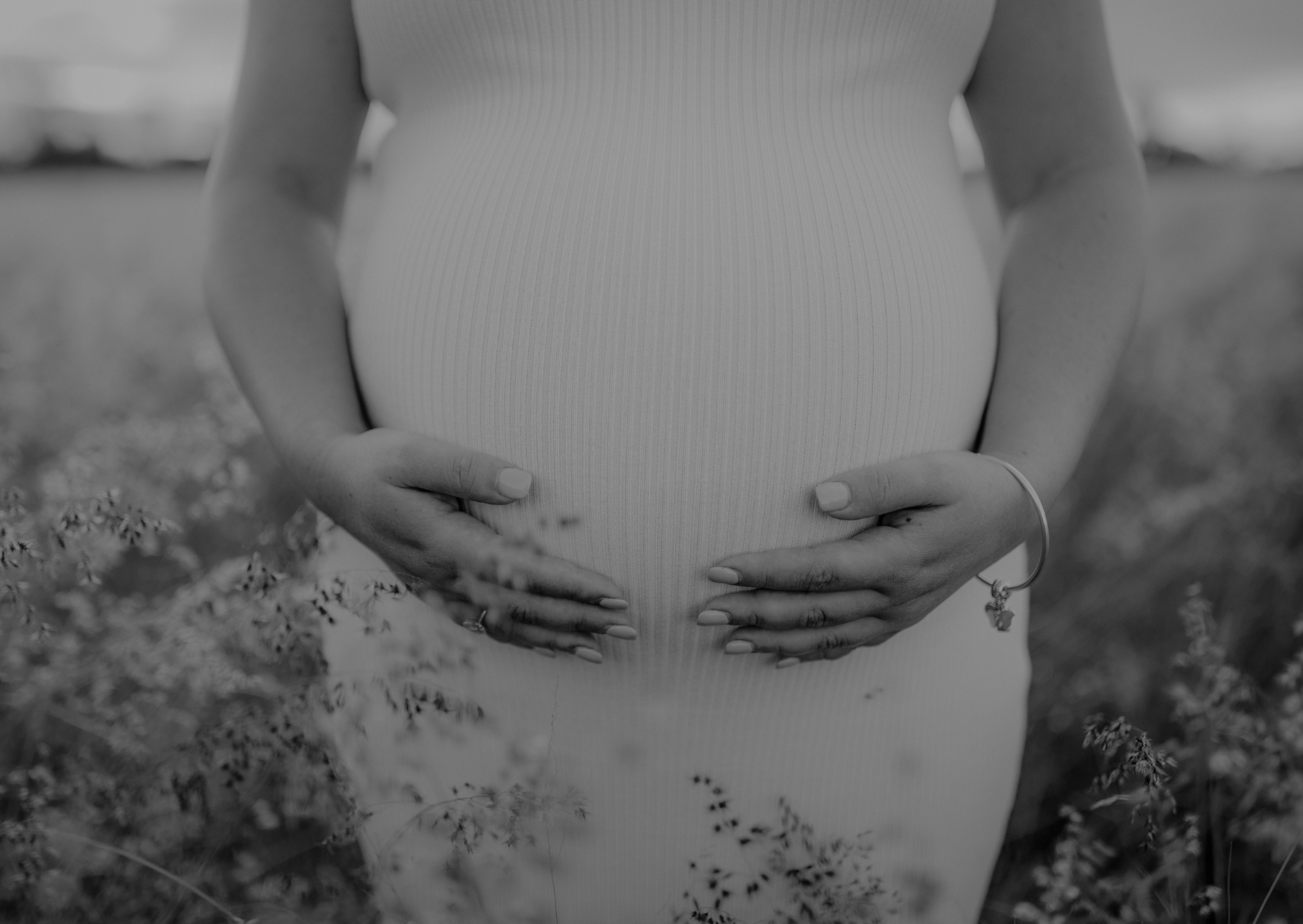Black and white photo of a pregnant person holding their belly in a natural setting