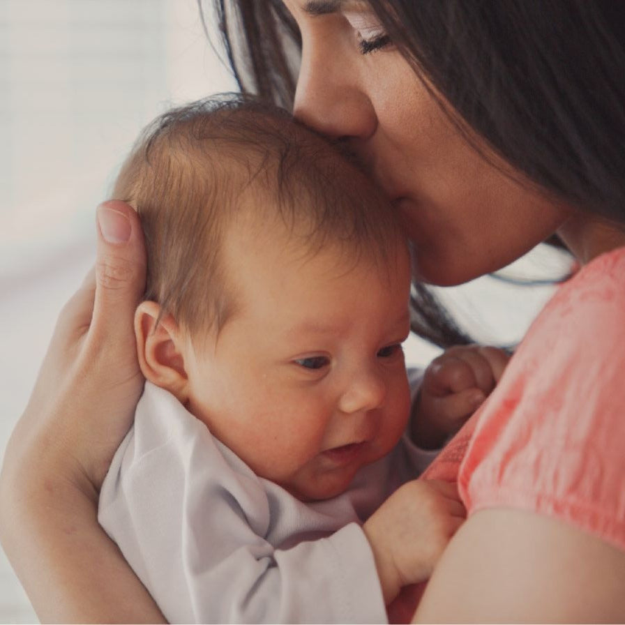 Woman holding and kissing a baby on the head with a blurred background