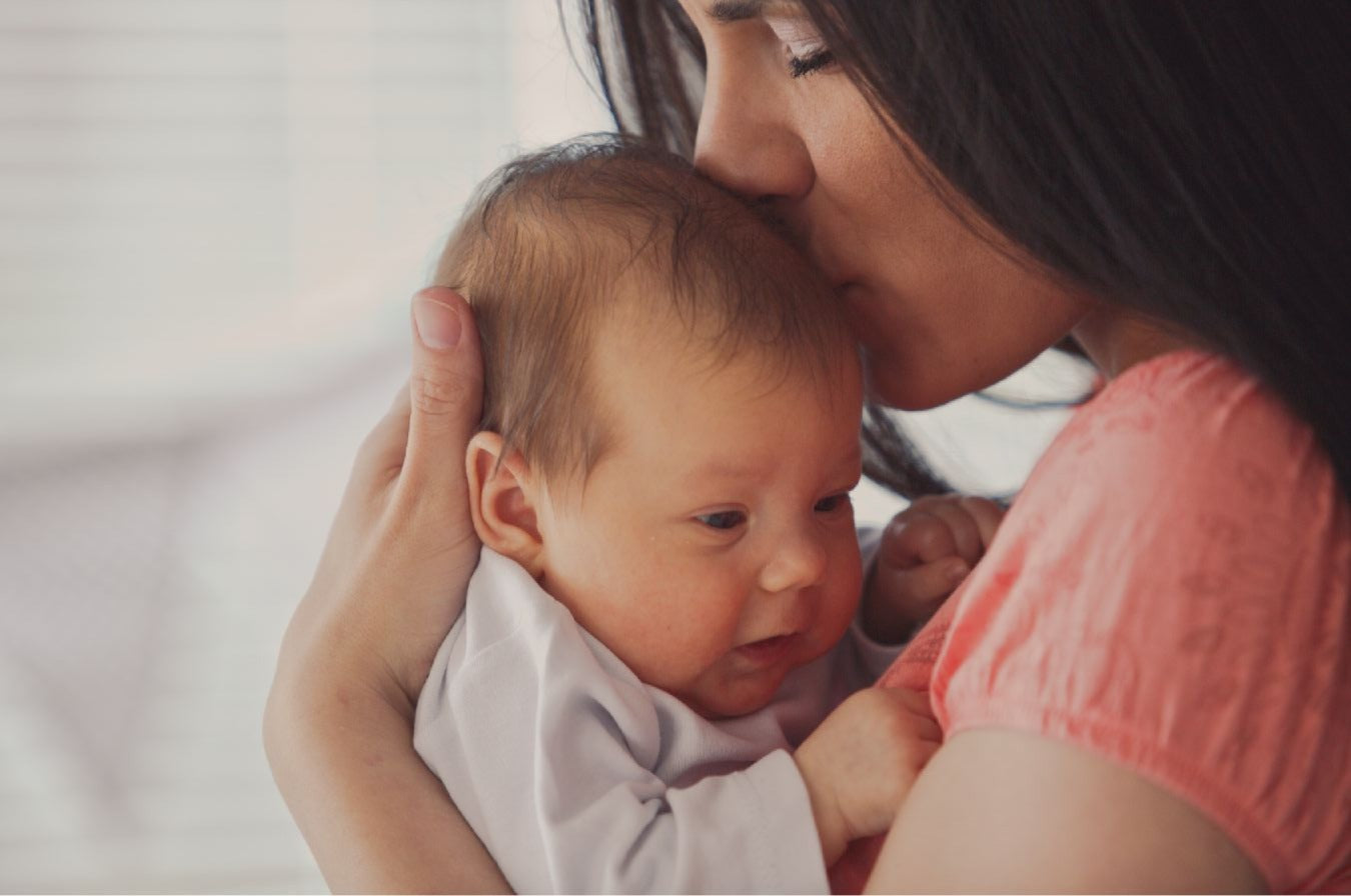Woman holding and kissing a baby on the head with a blurred background