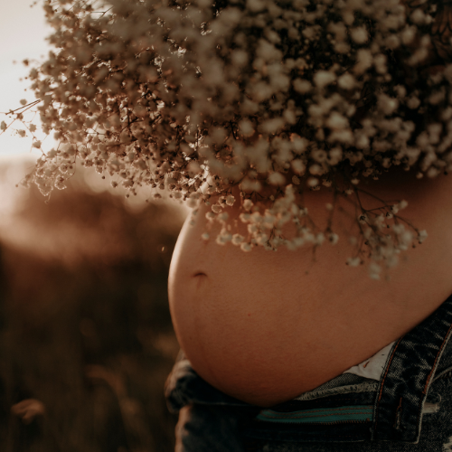 Pregnant person holding a bouquet of flowers with a blurred natural background