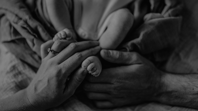 Close-up of a person's hands holding a baby's feet wrapped in a blanket