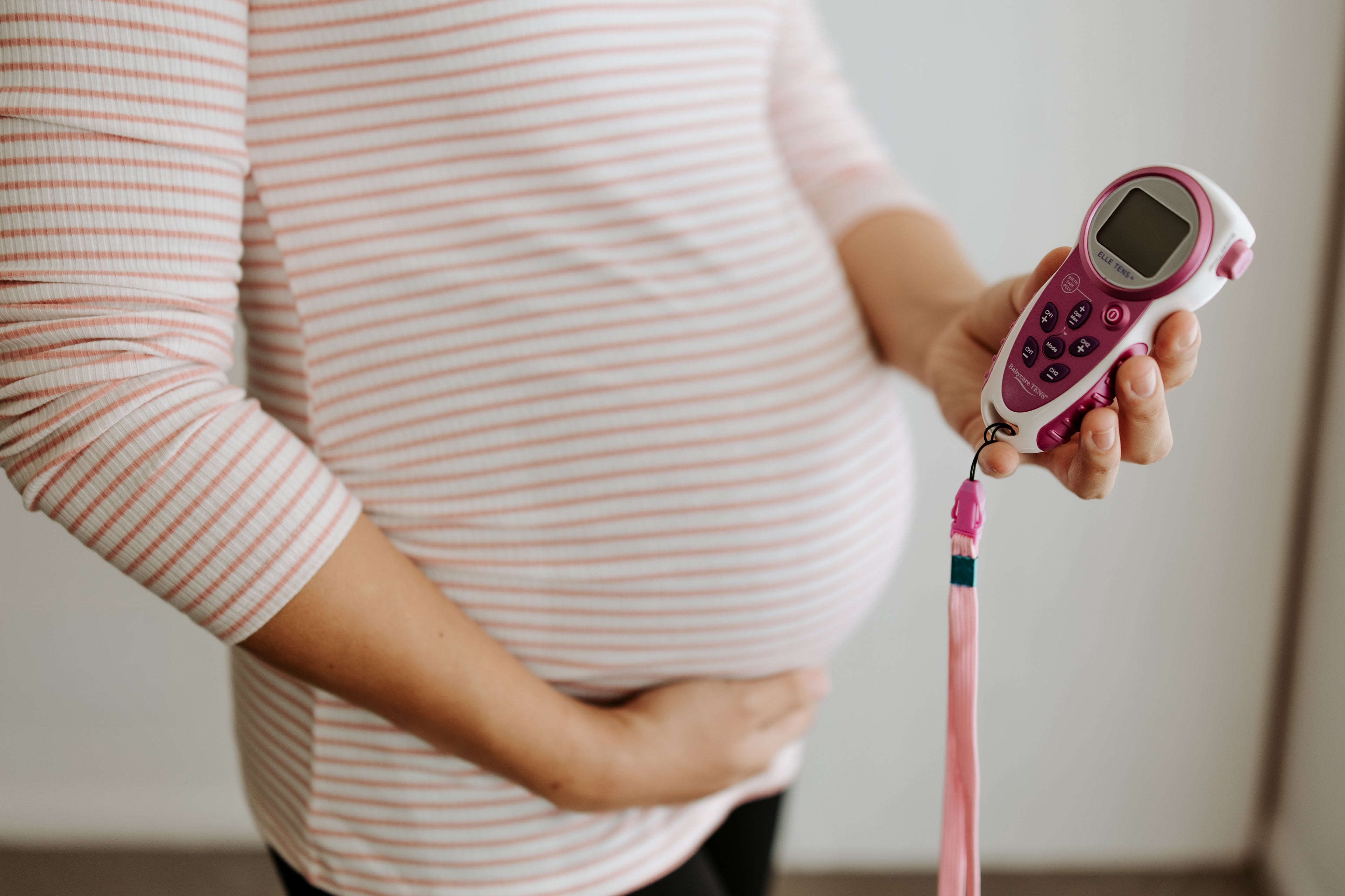 "Pregnant woman holding a TENS machine for labour pain relief, available from The Birth Teacher in Emerald QLD"