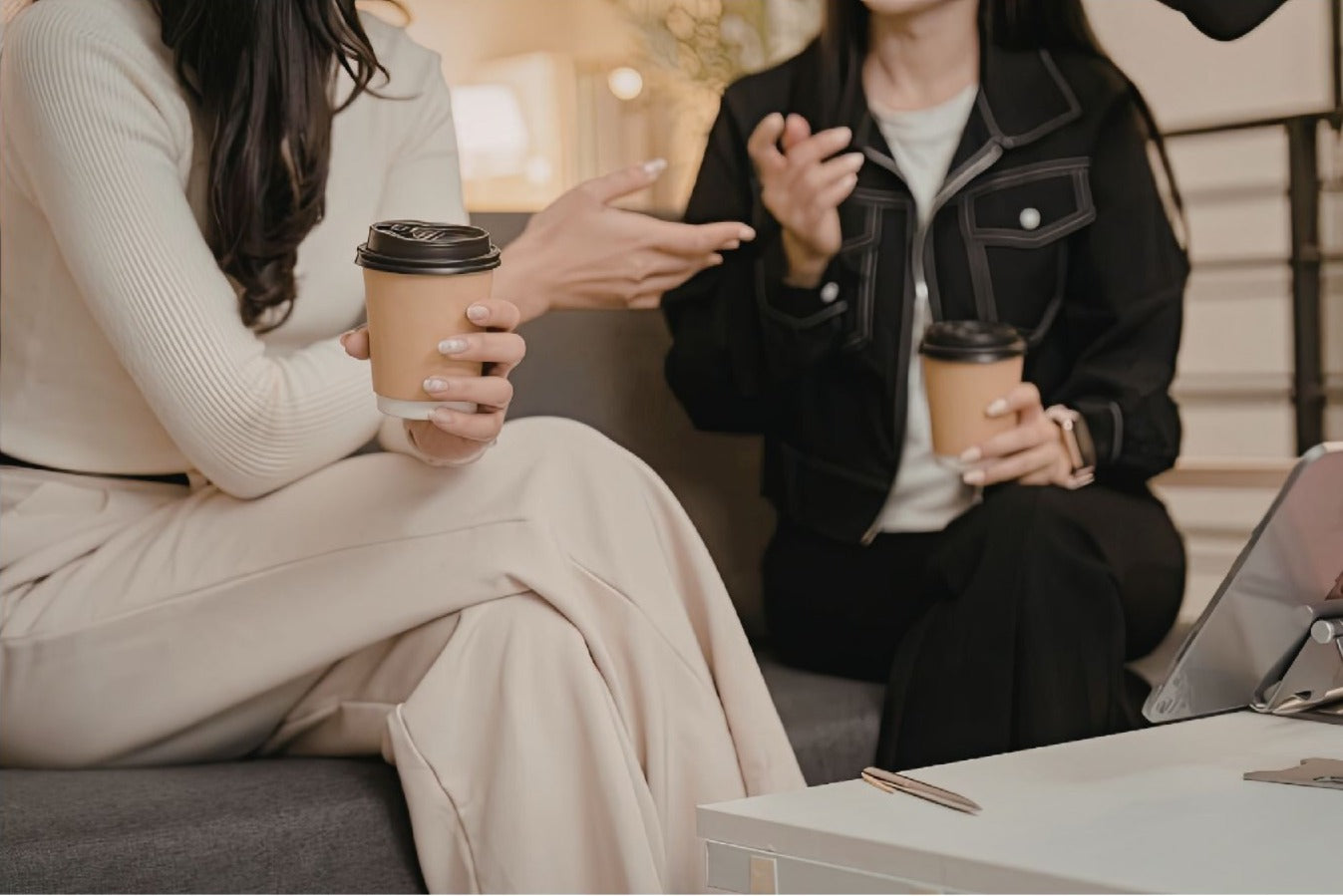Two people sitting on a couch holding coffee cups, engaged in conversation.